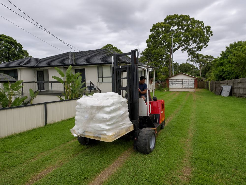 Quickcargo moffett forklift delivering a pallet of bagged building materials across a residential site
